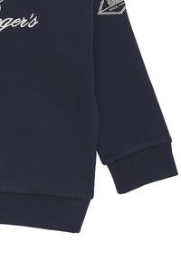 Felpa blu navy con polsini e orlo a coste, presenta testo ricamato bianco e una piccola etichetta con logo sulla manica. Tessuto soffice e texturizzato.