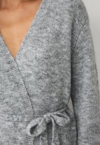 Cardigan grigio a maglia con scollo a V profondo, maniche lunghe e dettaglio in vita annodato, realizzato in un morbido tessuto testurizzato con un motivo sottile.