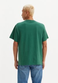 Grønn bomull T-skjorte med avslappet passform, korte ermer og rett kant, kombinert med blå denim bukser. Glatt, ensfarget tekstur.