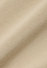 Beżowa, teksturowana tkanina z plecionym wzorem, prezentująca miękki, średniej wagi materiał o subtelnym połysku. Idealna na odzież lub tapicerkę.