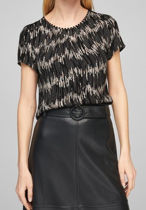 Kobieta ubrana w czarną, wzorzystą bluzkę z krótkim rękawem oraz czarną, wysokowarstwową spódnicę z eko skóry z paskiem z okrągłą klamrą.