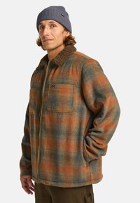 Geruit jasje in oranje, blauw en bruine tinten, met een bruin bonten kraag, twee voorzakken en een ritsluiting.