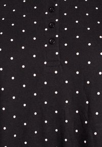 Camisa polo negra con lunares blancos, con una abertura con botones y una textura de tela suave. Los botones son negros y están espaciados uniformemente.