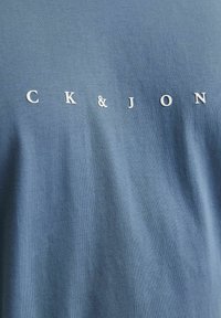 Blå bomuld T-shirt med hvid tekst "CK & JON" tværs over brystet. Stoffet har en glat tekstur og en afslappet pasform.