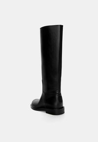 Botte en cuir noir, hauteur genou, avec une texture lisse, un bout rond et un design minimaliste. Talon bas et plat ; détail de couture latérale visible.