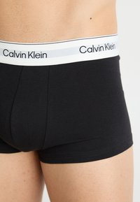 Zwarte katoenen boxershorts met een aansluitende pasvorm. De witte tailleband heeft het "Calvin Klein"-logo in het zwart tegen een zilveren streep.