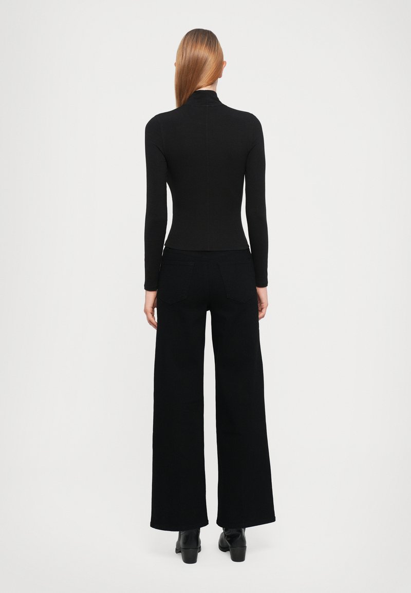 Haut noir à manches longues avec un col montant, associé à un pantalon noir à jambes larges. Texture lisse, ajusté à la taille et détails minimalistes.