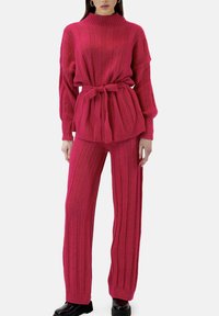 Różowy sweter z dzianiny z wysokim kołnierzem i paskiem w talii, w połączeniu z pasującymi szerokimi spodniami o pionowej prążkowanej fakturze na całej powierzchni.