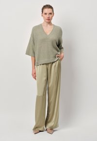 Lichtgroene, oversized gebreide trui met een V-hals; gecombineerd met hooglopende, wijde, glanzende beige satijnen broeken. Puntaarde beige schoenen.