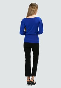 Top de punto azul con escote redondeado y mangas abullonadas, combinado con unos pantalones de mezclilla negros acampanados con borde de encaje en el dobladillo. Los tacones negros completan el look.