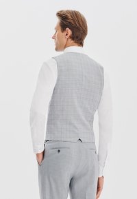 Jasnoszary kamizelka w kratę, dopasowany krój i gładka tekstura, zestawiona z białą koszulą i szarymi spodniami.