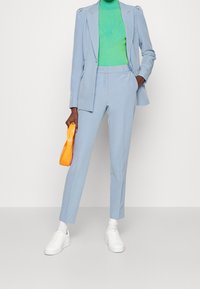 Ljusblå skräddarsydd kostym med slim fit-byxor och blazer, ihopparad med en grön ribbad högkrage och vita sneakers. En orange väska som accent.