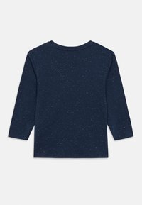 Granatowy, długorękawowy shirt z małymi białymi kropeczkami, okrągłym dekoltem i prostym dołem, ułożony płasko na białym tle.