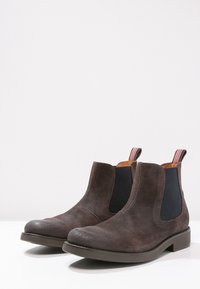 Bruine suède Chelsea boots met elastische zijkanten, gestructureerde afwerking, ronde neus en contrasterende lussen met een gestreept patroon.