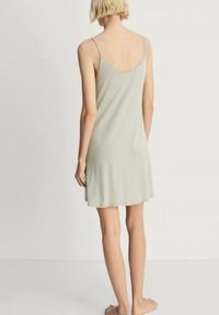 Ljusgrön mjuk tygnattklänning med spagettiband, utsvängd fåll och en enkel design, sedd bakifrån.