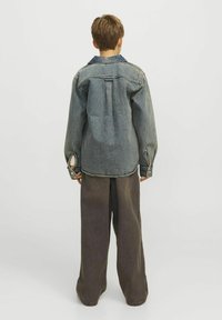 Jeansjacka med avslappnad passform, med en blå krage och långa ärmar, bärs över vida mörka byxor. Ljust blåtvätt, texturerad tyg.
