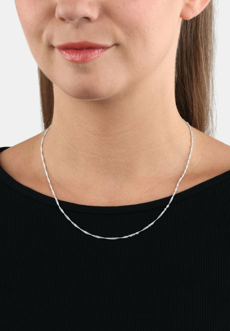 Silverfärgad kedja med en vriden design, bärs runt halsen ovanför en svart topp, med fin textur och polerad yta.