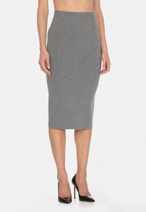 Falda lápiz de punto gris con cintura alta y costuras laterales, combinada con zapatos de tacón alto de charol negro. Textura suave y diseño ajustado.