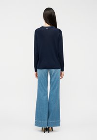 Μπλε ναυτικό τοπ με μακριά μανίκια και στρογγυλή λαιμόκοψη, σε συνδυασμό με ανοιχτό μπλε τζιν παντελόνι με φουσκωτά μπατζάκια και μαύρες ψηλές γόβες, από πίσω όψη.