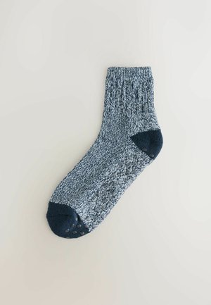 Chaussettes à cheville bleu et blanc avec un revers côtelé, un orteil et un talon bleu foncé, et des points de grip en caoutchouc sur la semelle pour la traction.