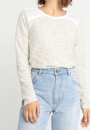 Lys grå striktrøje med tekstureret mønster, hvide skulderdetaljer, lange ærmer, båret med højtaljede lyseblå jeans.