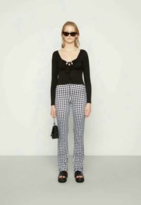 Top preto de mangas longas com um laço na frente, calças xadrez em preto e branco, sapatos de plataforma e uma pequena bolsa preta.