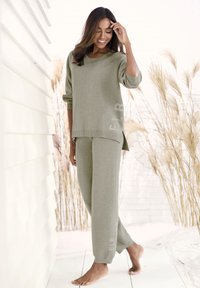 Graues Strick-Loungewear-Set mit einem locker sitzenden, gerippten Pullover und passenden, schmal zulaufenden Hosen, mit dezentem Branding an der Seite. Barfußmodell.