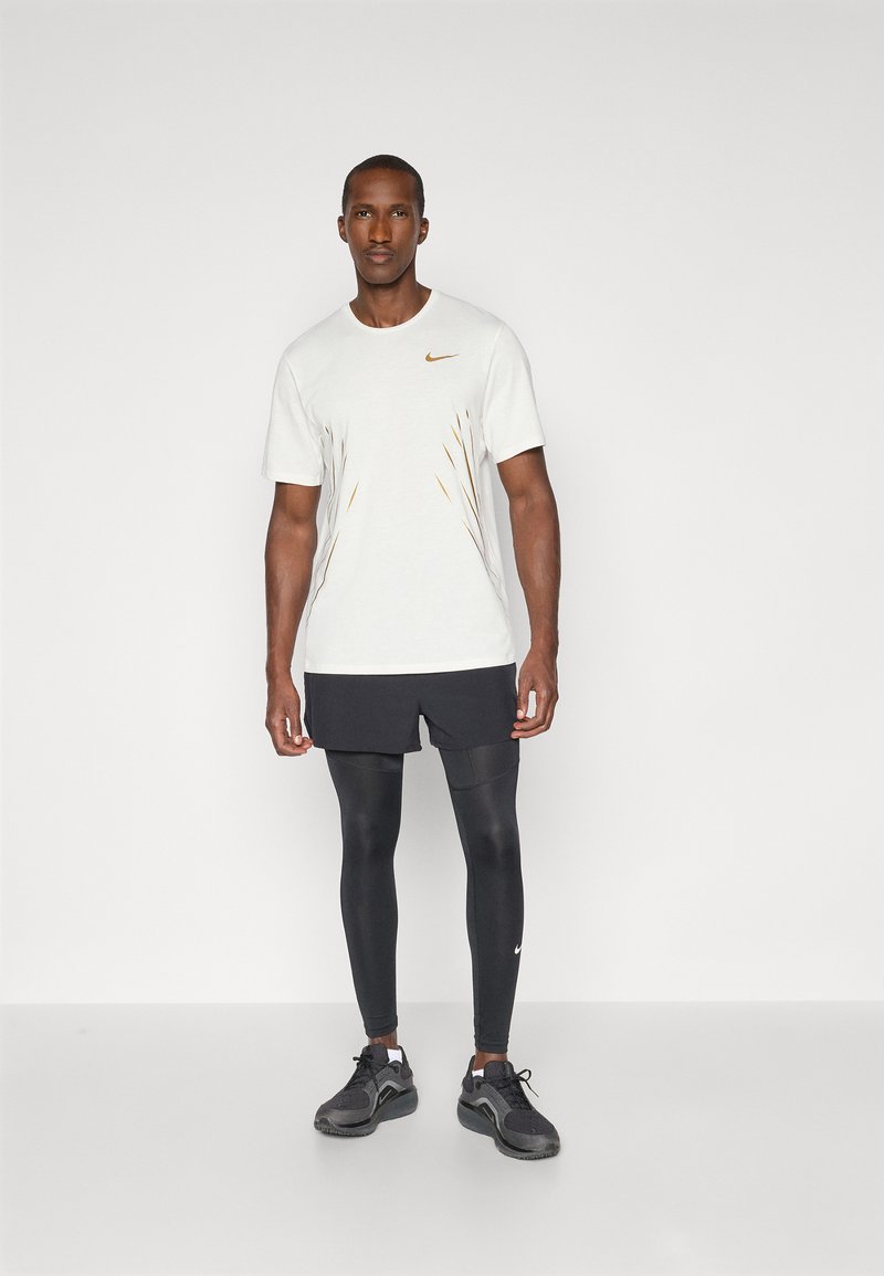 Stroje sportowe Nike składające się z jasnoszarej koszulki z krótkim rękawem z pomarańczowymi akcentami, czarnych szortów i czarnych legginsów. Czarne buty sportowe.