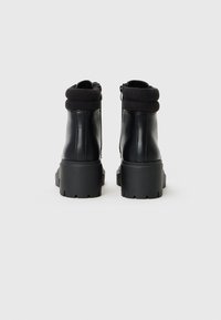 Bottines noires avec un extérieur en cuir, un revers en tricot côtelé, une fermeture éclair latérale, une semelle en caoutchouc épaisse et des détails texturés sur la semelle.