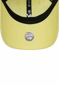 Gelbe Baseballmütze mit einem schwarzen Schirm, versehen mit einem runden MLB-Aufkleber mit einem Baseball-Graphik auf der Vorderseite. Strukturiertes Material, design mit fester Form.