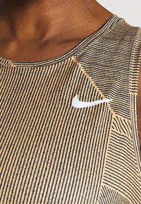 Gros plan d’une personne portant un débardeur Nike beige et noir à rayures avec le logo swoosh blanc sur la poitrine.
