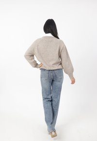 Maglione lavorato a maglia beige con scollatura a girocollo e maniche raglan, abbinato a jeans chiari a vita alta. L'outfit presenta una finitura texturizzata.