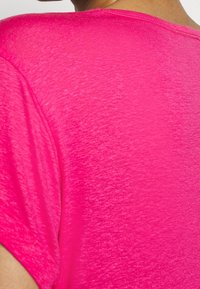 Camiseta de manga corta rosa en una tela ligera y texturizada. La parte posterior presenta un cuello redondo y un aspecto ligeramente jaspeado.