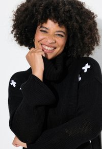 Schwarzer Strickrollkragensweater mit langen Ärmeln, der weiße Kreuzmuster an den Schultern und ein strukturiertes Maschenmuster aufweist.