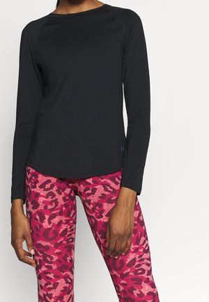 Woman wearing a fitted black long-sleeve shirt and bright pink patterned leggings with dark red leopard spots.