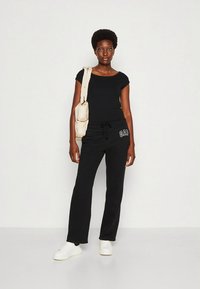 Svart topp med korta ärmar och svarta mysbyxor med dragsko, med en "GAP"-logotyp. Vita sneakers och en beige axelväska.