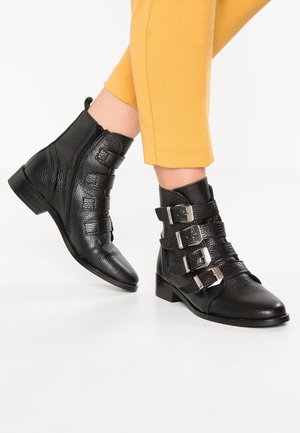 Bottes noires à la cheville en cuir texturé, dotées de trois boucles métalliques, d'une fermeture éclair sur le côté et d'un petit talon carré. Formées avec un bout pointu.