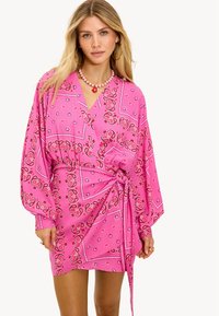 Robe portefeuille rose avec un imprimé cachemire, manches longues, encolure en V et taille ceinturée pour une silhouette ajustée. Texture de tissu douce.