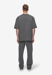 Übergroßes graues Baumwoll-T-Shirt mit kurzen Ärmeln, kombiniert mit passenden grauen Hosen, die einen lässigen Schnitt und ein minimalistisches Design aufweisen.