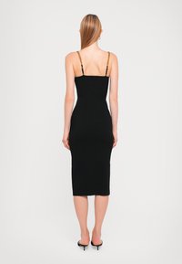Black midi dress with thin straps featuring gold chain accents. Fitted design, smooth texture, and a knee-length hem. Minimalistic style.