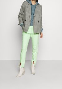 Blazer cruzado de cuadros grises, sudadera con capucha en color teal y pantalones ajustados verde menta con aberturas laterales. Completado con botas de tacón crema.
