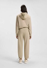 Beige huva jacka med en kortad design och elastiska manschetter, kombinerad med matchande joggerbyxor med ingefärsfötter och sidofickor.