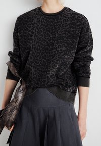 Sweatshirt noir avec un motif léopard, col et poignets côtelés, associé à une jupe plissée foncée et un sac à bandoulière marron.
