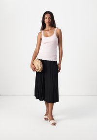 Top in magenta con bordi ondulati, abbinato a una gonna plissettata nera. Tiene una borsa beige e indossa sandali crema a scivolo.
