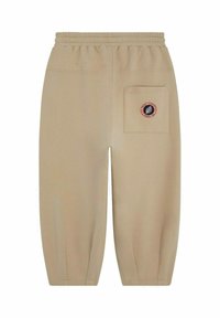 Pantalons de survêtement beiges avec une taille élastique, des poignets fuselés et une poche arrière arborant un patch logo circulaire rouge et bleu.