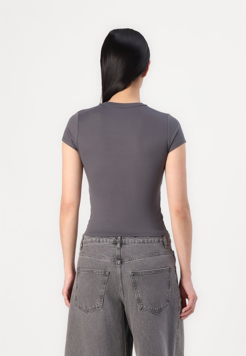 Graues, eng anliegendes T-Shirt mit kurzen Ärmeln, glattem Stoff und runder Ausschnittform, kombiniert mit grauen weit geschnittenen Jeans, die über Gesäßtaschen verfügen.