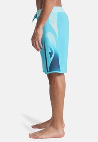 Τυρκουάζ βερμούδες με διαβάθμιση χρώματος· διαθέτουν ελαστική μέση με κορδόνι και πλαϊνή τσέπη. Το ύφασμα φαίνεται ελαφρύ και λείο.