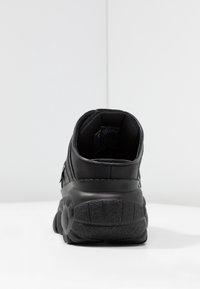 Svart sneaker med ovandel i läder, vadderad krage och texturerad gummisula. Utvecklad med rund klack och minimalistiska designelement.