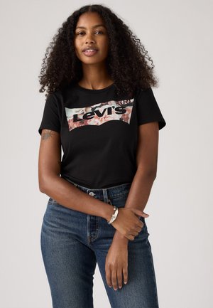 Juodas medvilninis trikotažas su gėlių Levi's logotipo dizainu. Apvalus kaklas, trumpomis rankovėmis, derinamas su mėlynomis džinsinėmis kelnėmis.