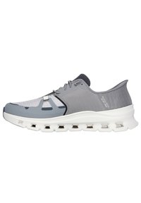 Zapatilla deportiva gris con parte superior de malla, suela blanca acolchada con recortes y un diseño aerodinámico. Acentos en tono gris más oscuro en el talón.